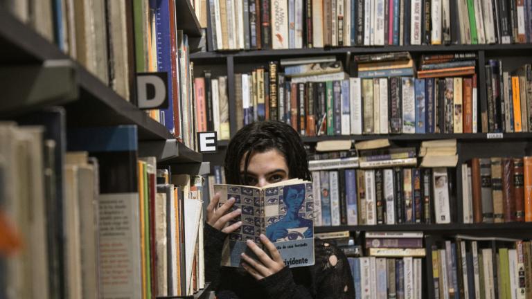 Mujer joven cubierta por un libro en una biblioteca